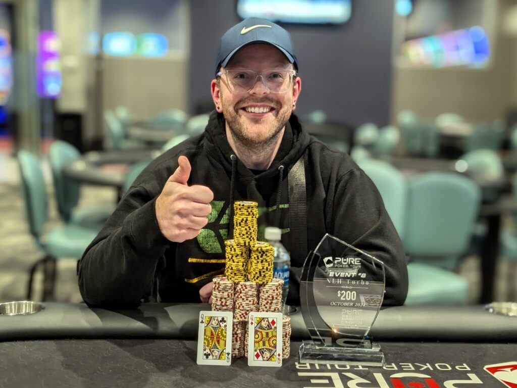 Deven Lane smiling person with thumb's up sitting in front of poker chips and a trophy after winning an event